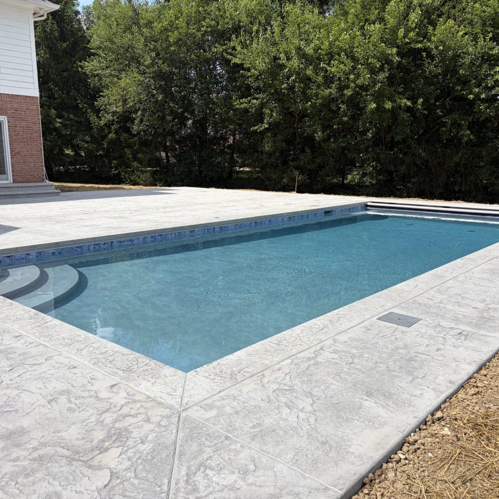 Contemporary inground pool featuring clean lines, a stamped concrete surround, and a large private backyard with mature landscaping