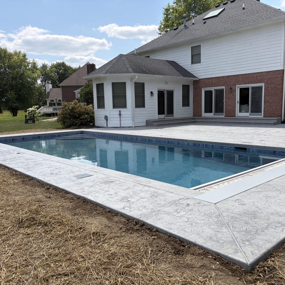 Modern rectangular inground swimming pool with a light gray stamped concrete patio
