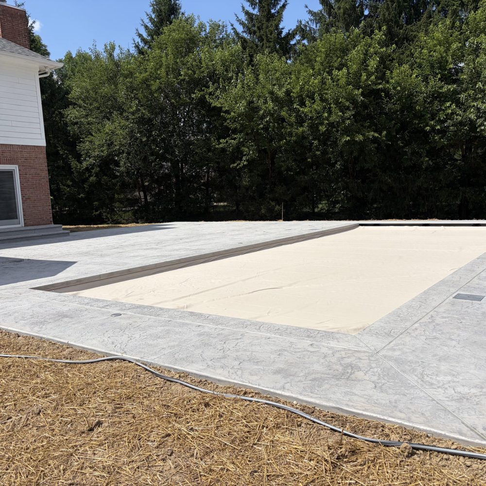 Wide view of a newly installed rectangular inground pool with an expansive stamped concrete patio and landscaped backyard